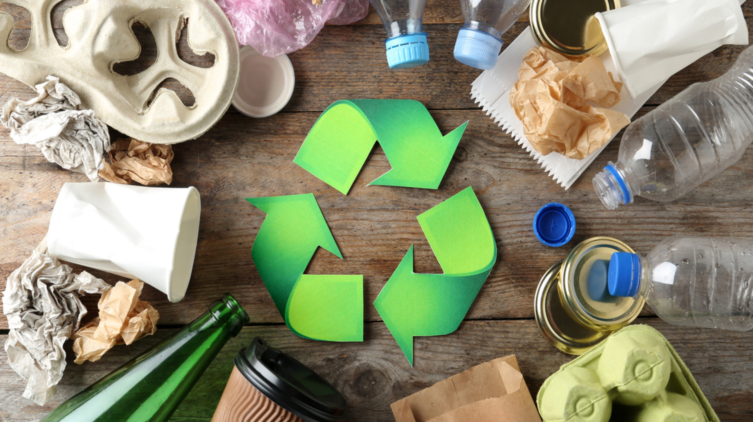 Recycling symbol and different garbage on wooden background, top view
