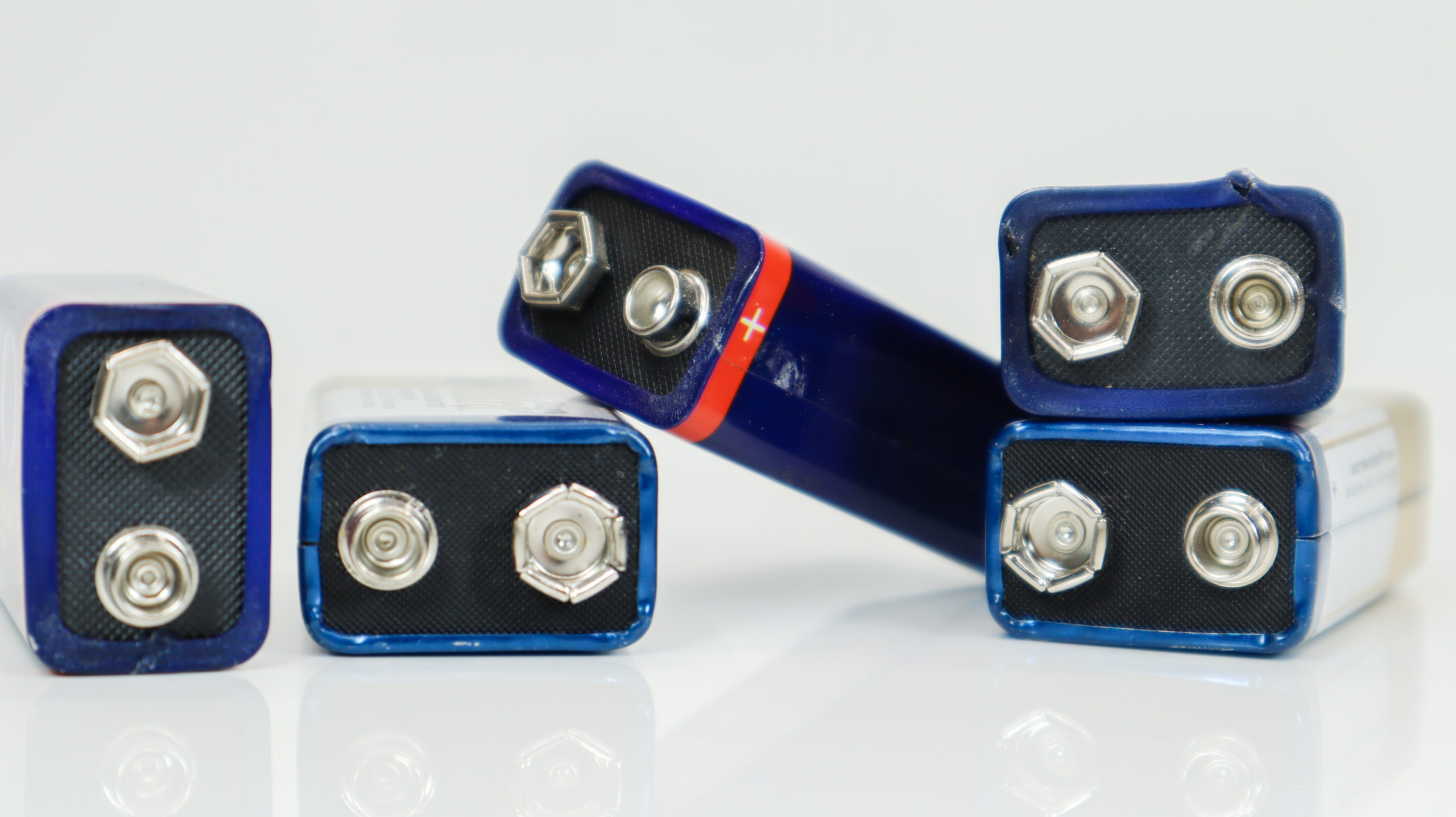 Five blue used, chaotically laid out and scattered PP3 batteries on a white background with reflection. Main battery for personal power supplies. Close-up of a scratched and used battery connector.